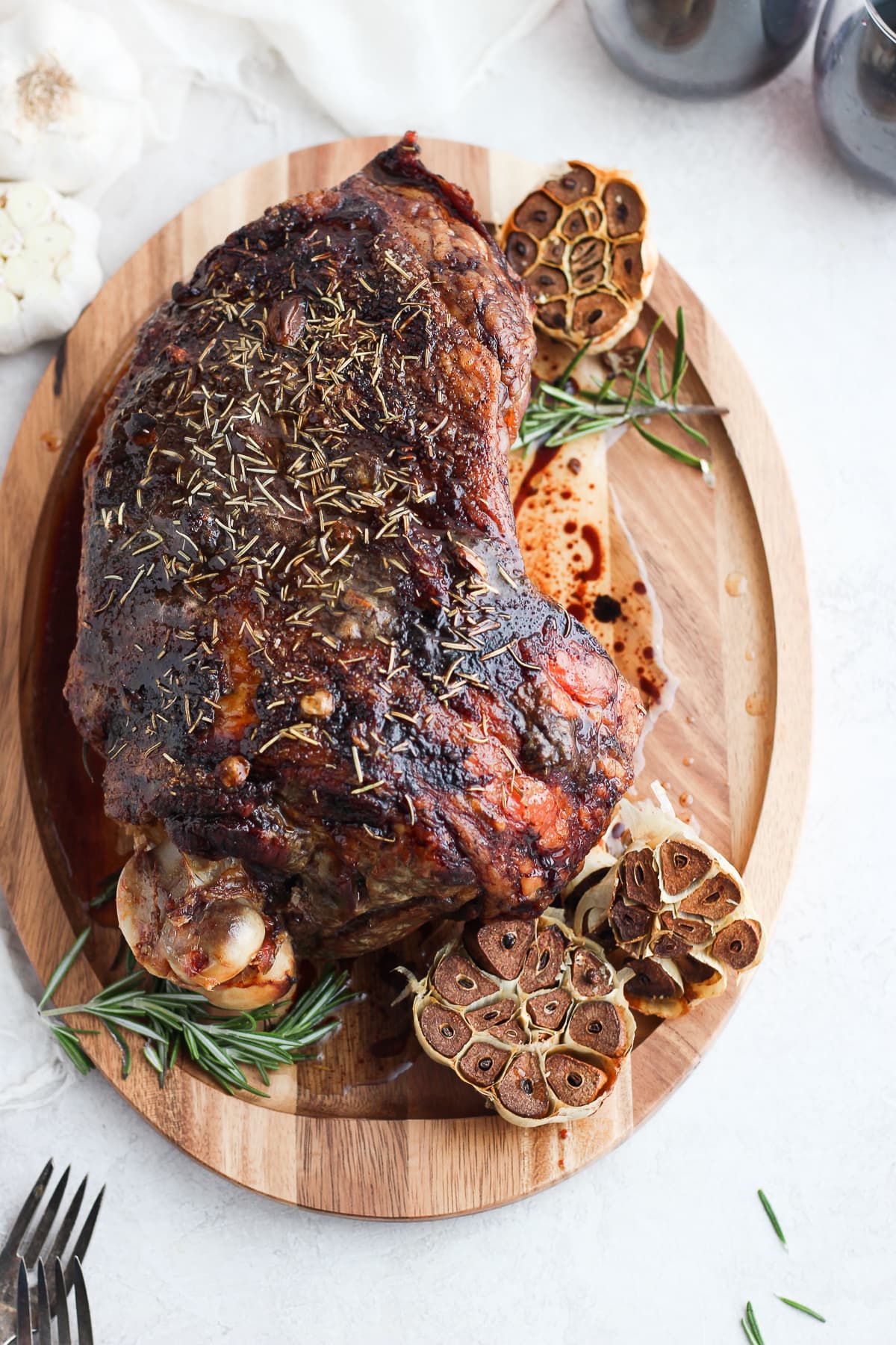 Roasted Rosemary Garlic Leg of Lamb on a cutting board with two glasses of red wine in the background. 