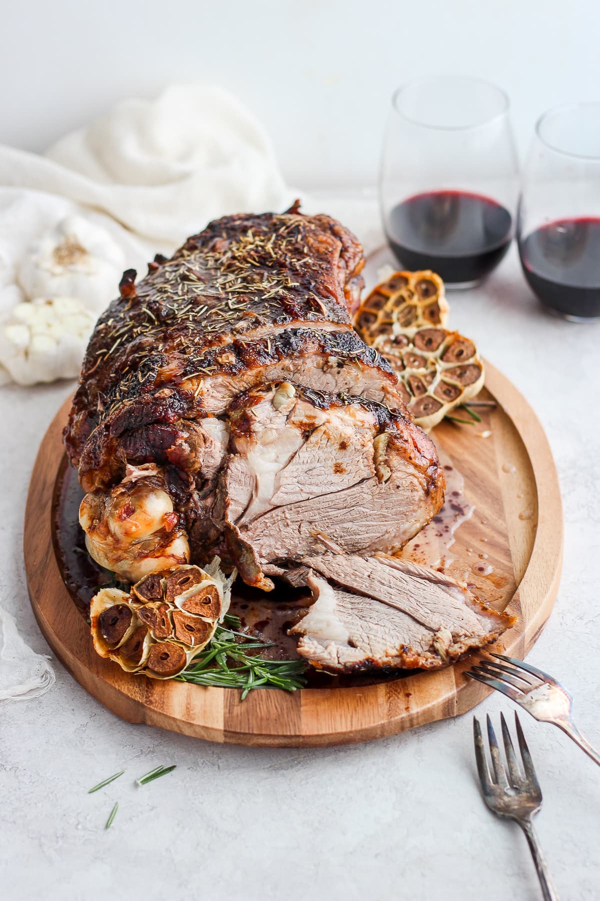 Roasted Rosemary Garlic Leg of Lamb on a cutting board with two glasses of red wine in the background. 