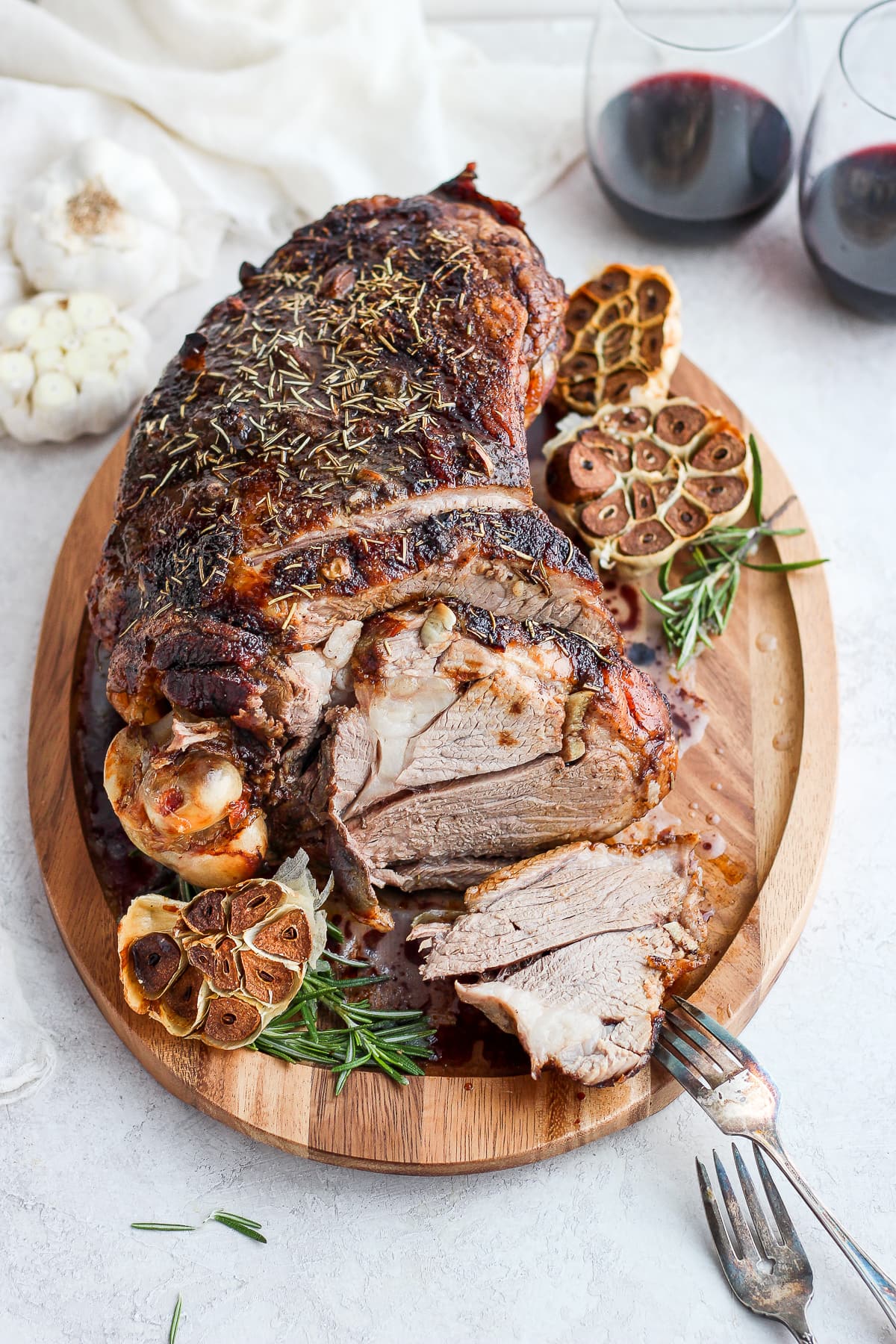 Roasted Rosemary Garlic Leg of Lamb on a cutting board with two glasses of red wine in the background. 