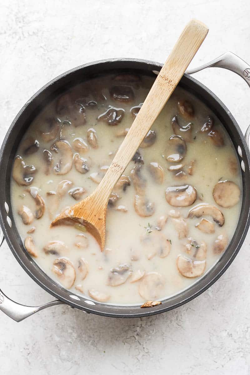 Homemade dairy free cream of mushroom soup in a black pot with a wooden spoon sticking out.