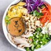 A chopped rotisserie chicken salad in a white bowl with a small dish of dressing.