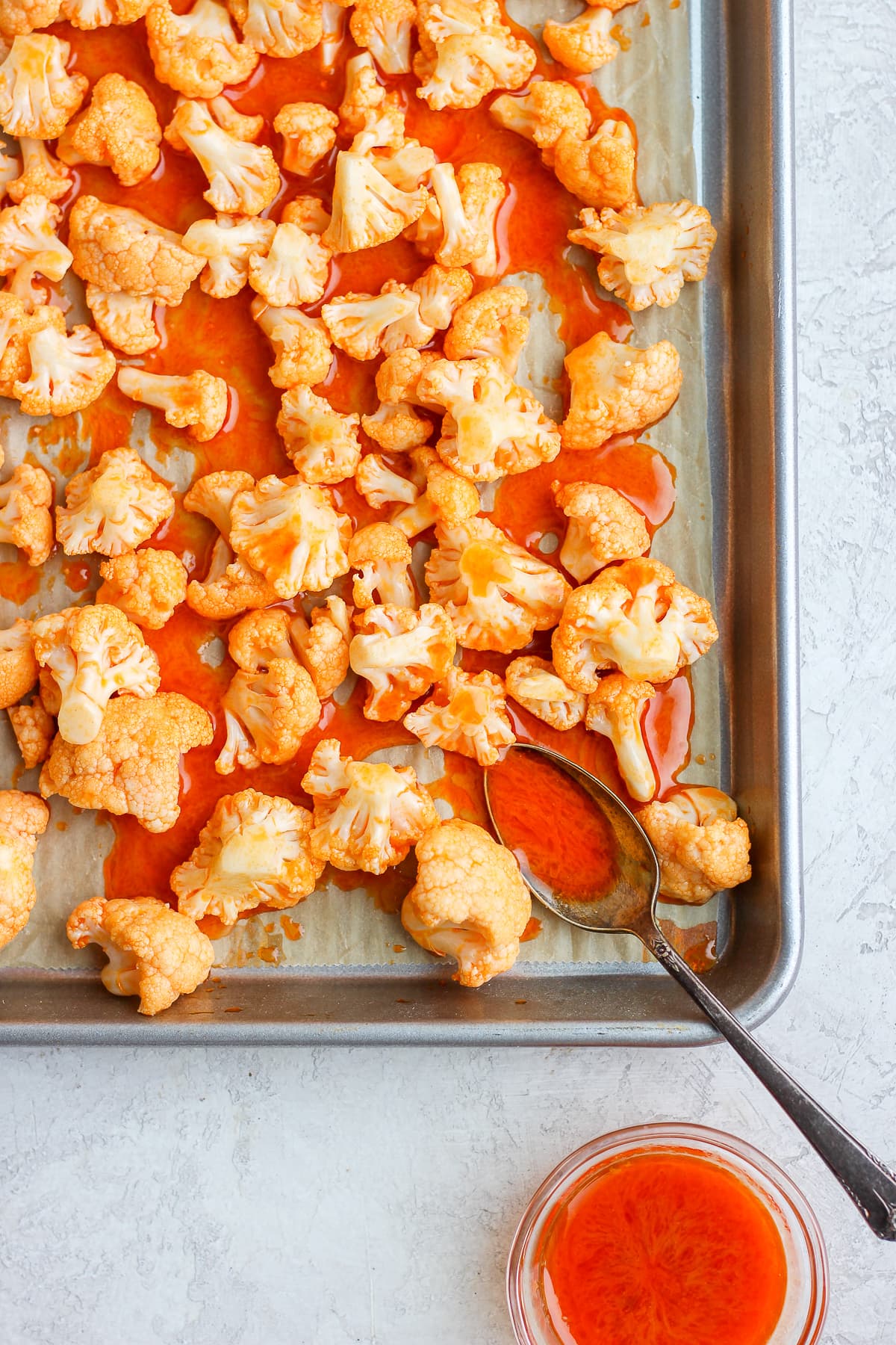 Cauliflower covered in buffalo sauce on a parchment-lined baking sheet.