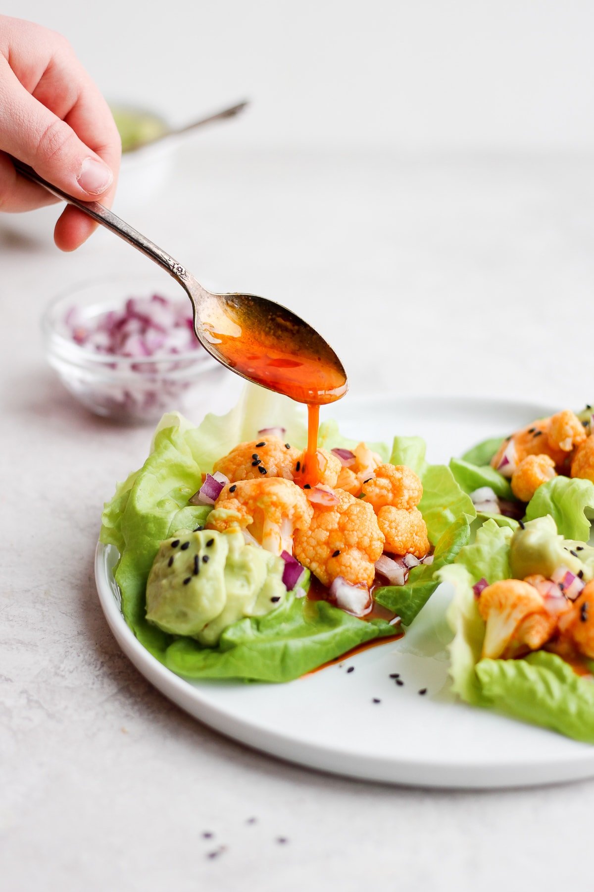 More buffalo sauce being poured from a spoon onto a cauliflower lettuce wrap.