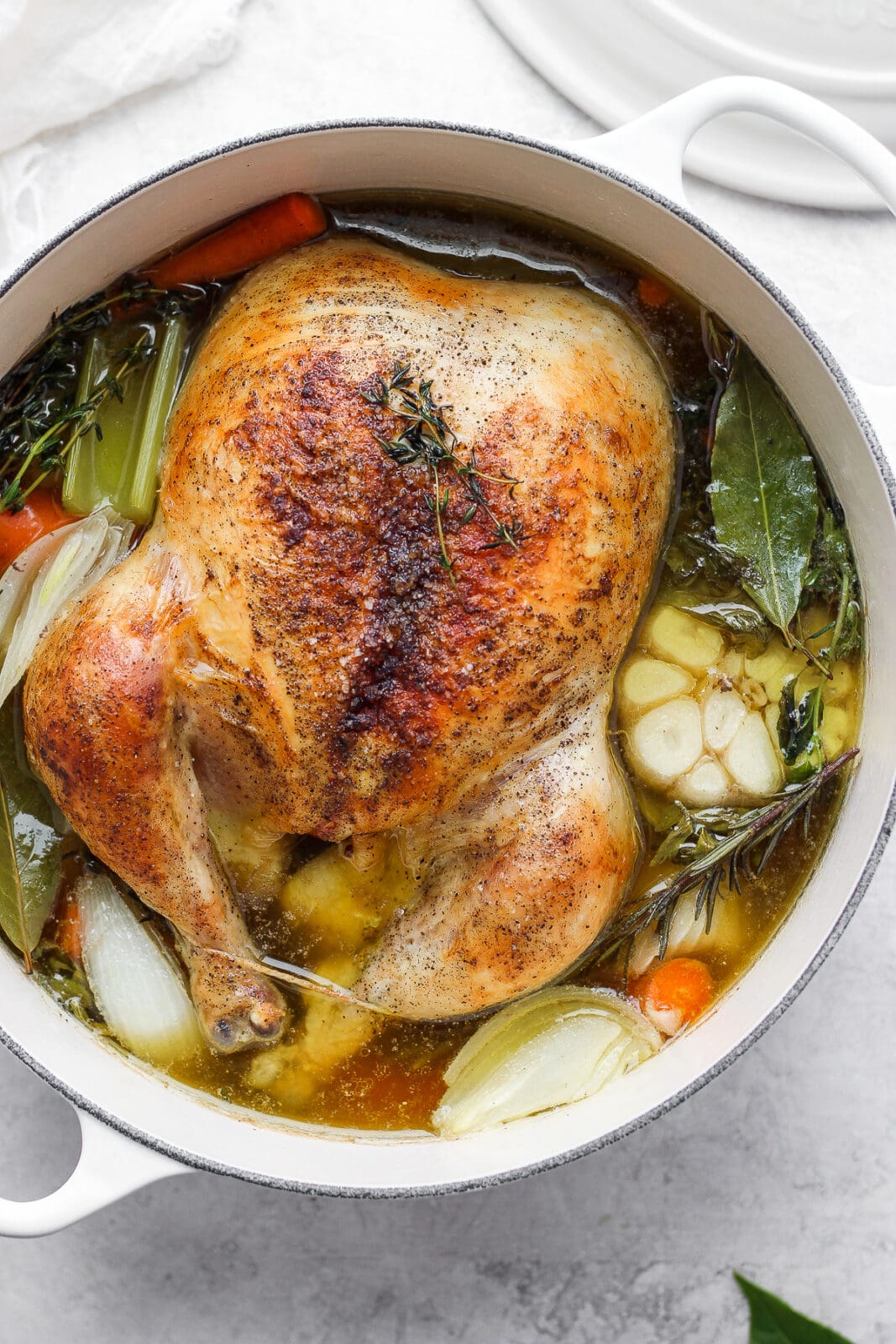 Dutch Oven with a roasted chicken inside surrounded by broth, vegetables and herbs.