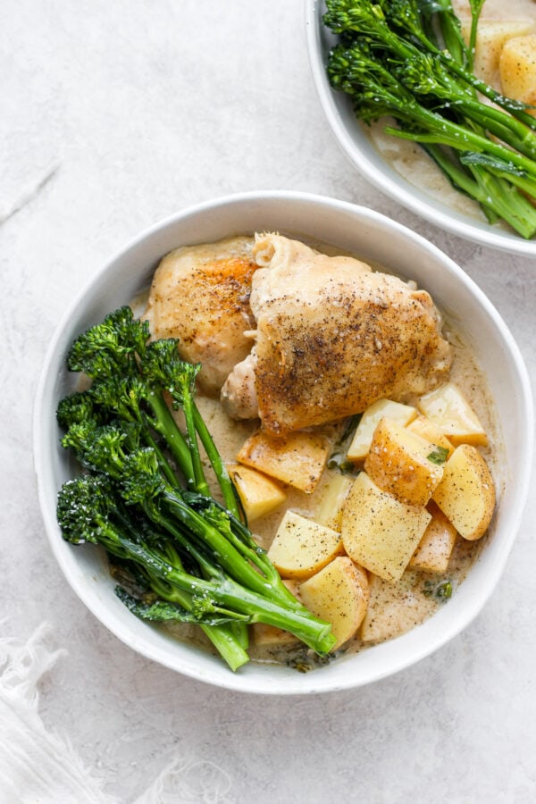 A bowl full of dairy free dijon chicken with broccolini next to another bowl of dijon chicken with broccolini.