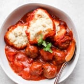 Gluten free meatballs and dumplings in a white bowl with a spoon in the side.