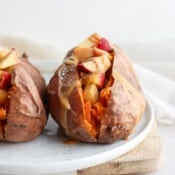 Two cooked sweet potatoes stuffed with apples and cashew butter on a white plate.