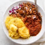 A bowl of spaghetti squash, ground pork and marinara sauce with a spoon sticking out.
