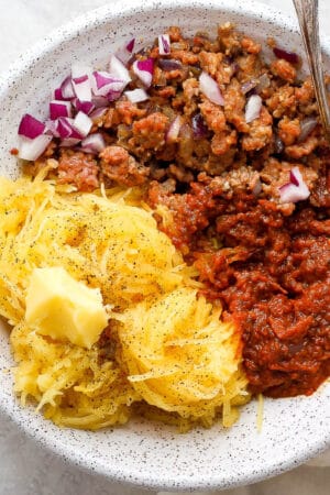 A bowl of spaghetti squash, ground pork and marinara sauce with a spoon sticking out.