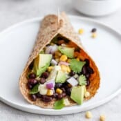A white plate with a black bean and avocado wrap.