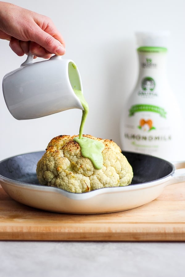 Avocado sauce being poured over a roasted head of cauliflower.