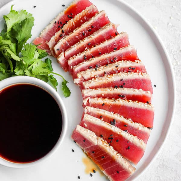 A plate of seared ahi tuna with cilantro and a little bowl of dipping sauce.