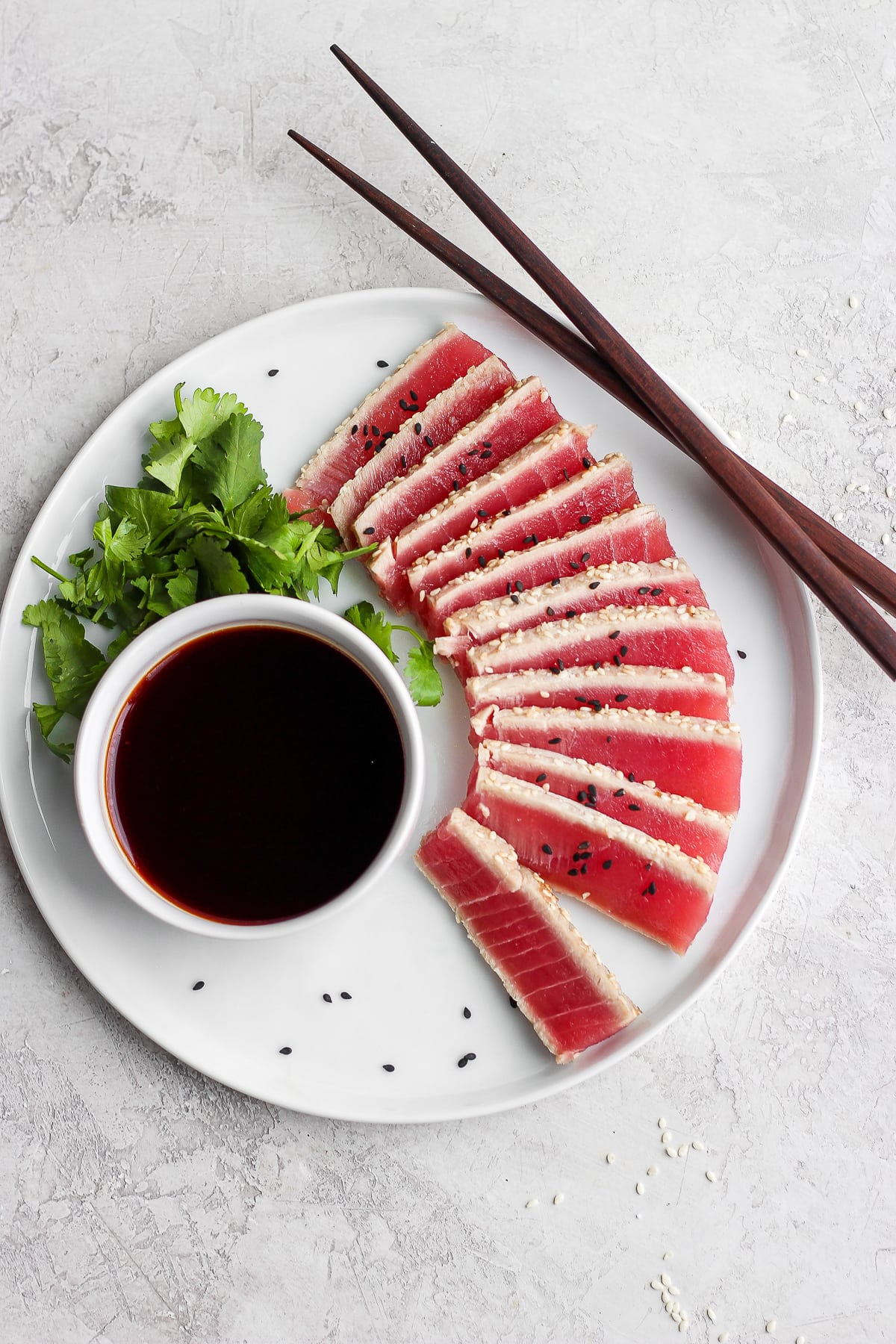 Sliced ahi tuna with soy sauce and cilantro on a white plate. 