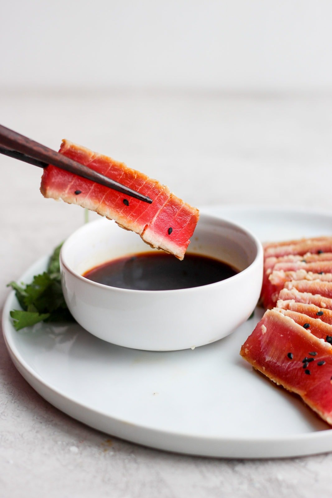 A piece of seared ahi tuna being dipped into a bowl of soy sauce with chopsticks. 
