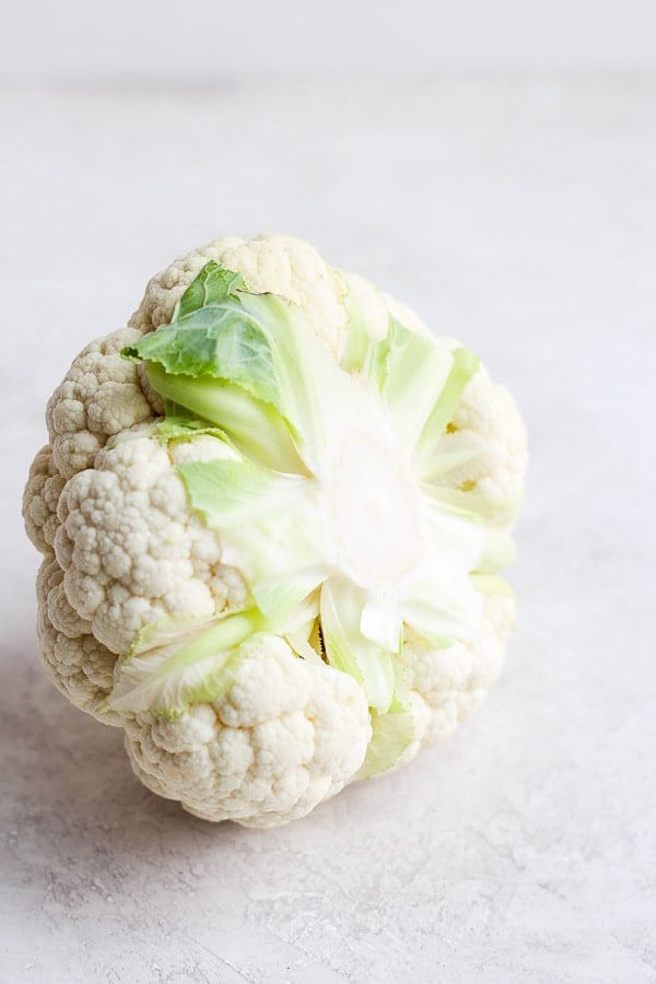 A whole cauliflower with part of the stem removed so that it is flat.