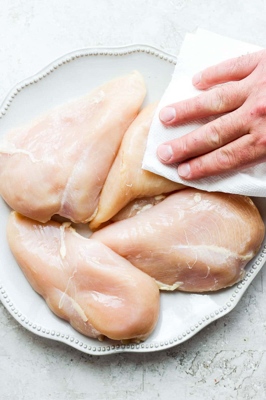 Someone patting dry a plate of raw chicken breasts.