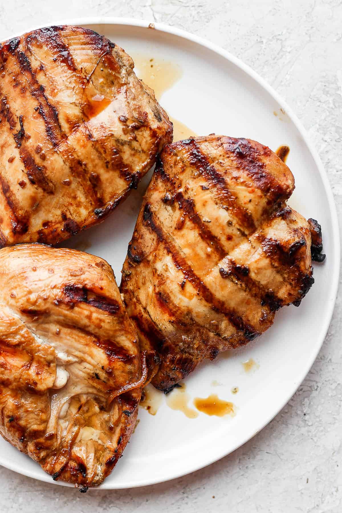 Three chicken breasts on a plate that have just been grilled. 