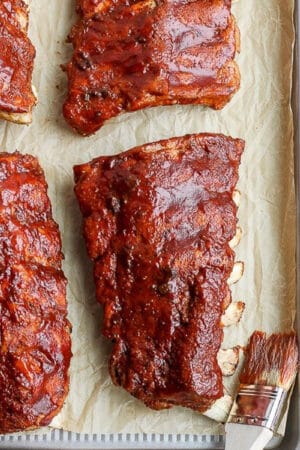 A parchment lined baking sheet with ribs covered in bbq sauce that have been cooked in an Instant Pot or pressure cooker.
