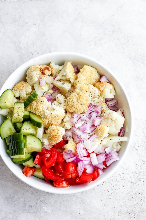 All the fresh vegetables mixed in a large white bowl with salt and pepper on top.