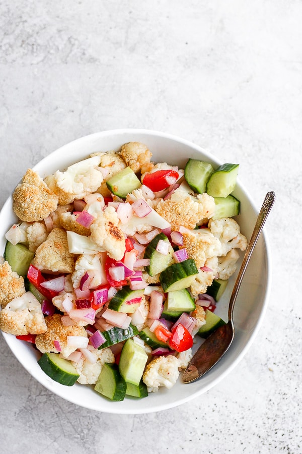 Roasted cauliflower salad in a large white bowl with a spoon.