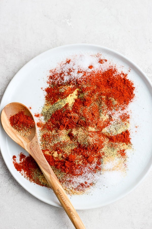 A plate with pork shoulder dry rub ingredients on it and wooden spoon. 