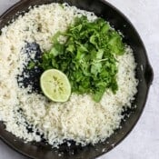 Cooked cauliflower rice in a cast iron skillet with fresh cilantro and a half of a squeezed lime.