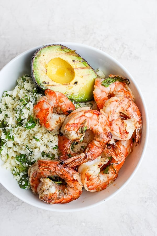 A white bowl with cilantro lime shrimp, cilantro lime cauliflower rice, and a grilled avocado.