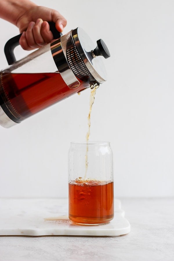 Someone pouring cold brew coffee out of a French press and into a glass. 