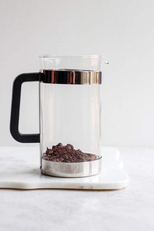 A glass French press with roughly ground coffee beans at the bottom. 