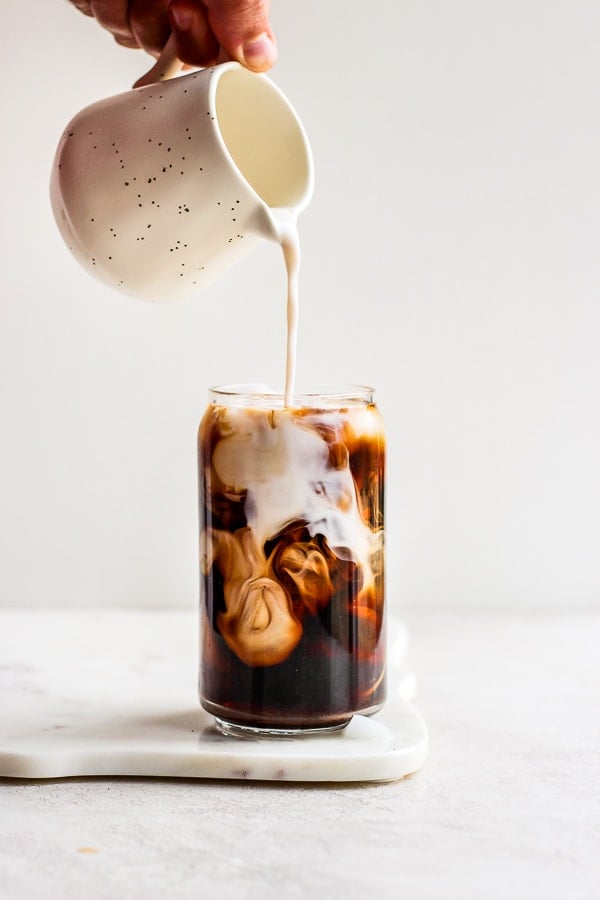 Someone pouring almond milk into a glass of French press cold brew coffee. 