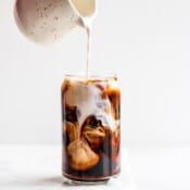 Creamer being poured into a glass of cold brew coffee made in a french press.