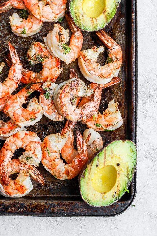 Grilled shrimp on a baking sheet with grilled avocado halves.