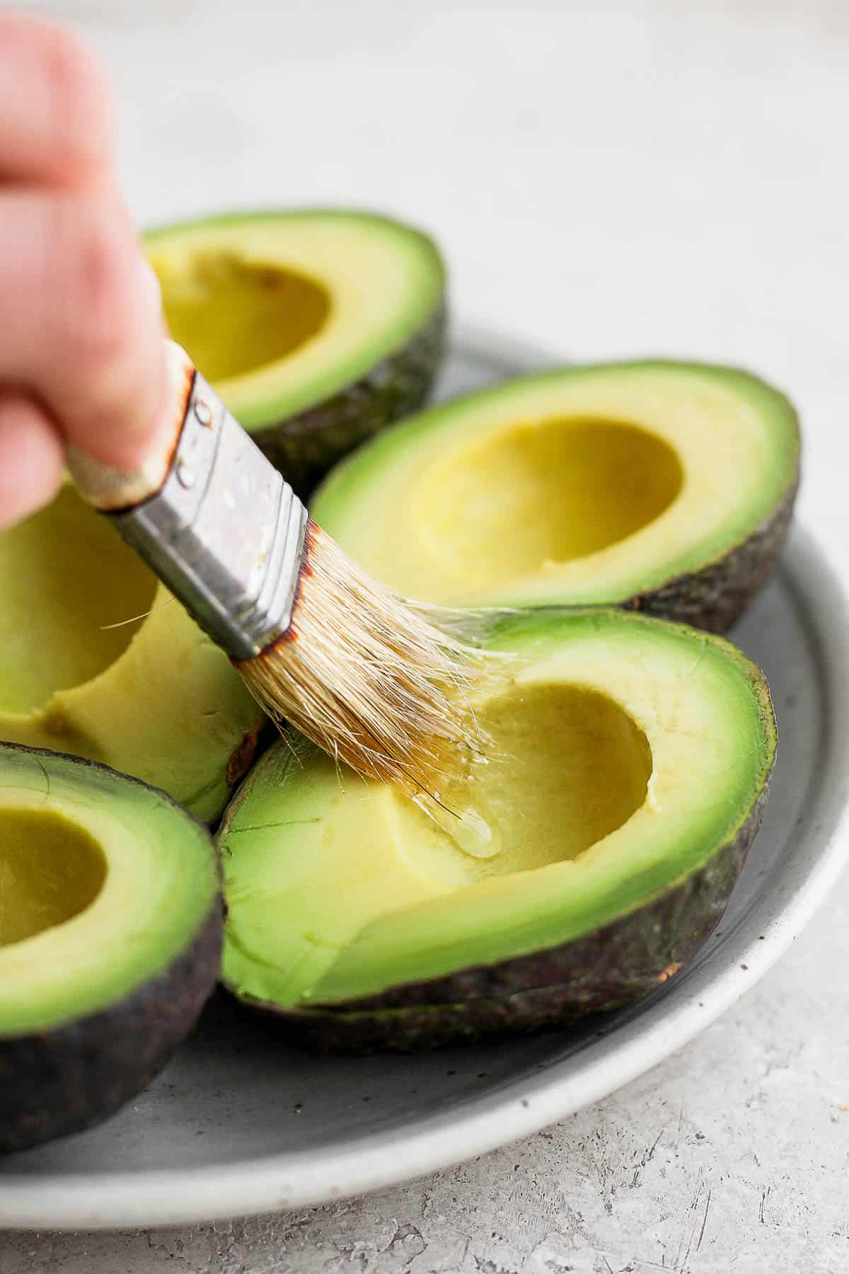 Someone brushing olive oil on a avocado half. 