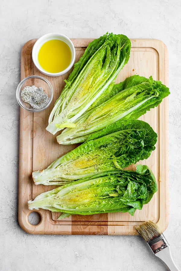 Romaine hearts on a cutting board with olive oil and salt/pepper.