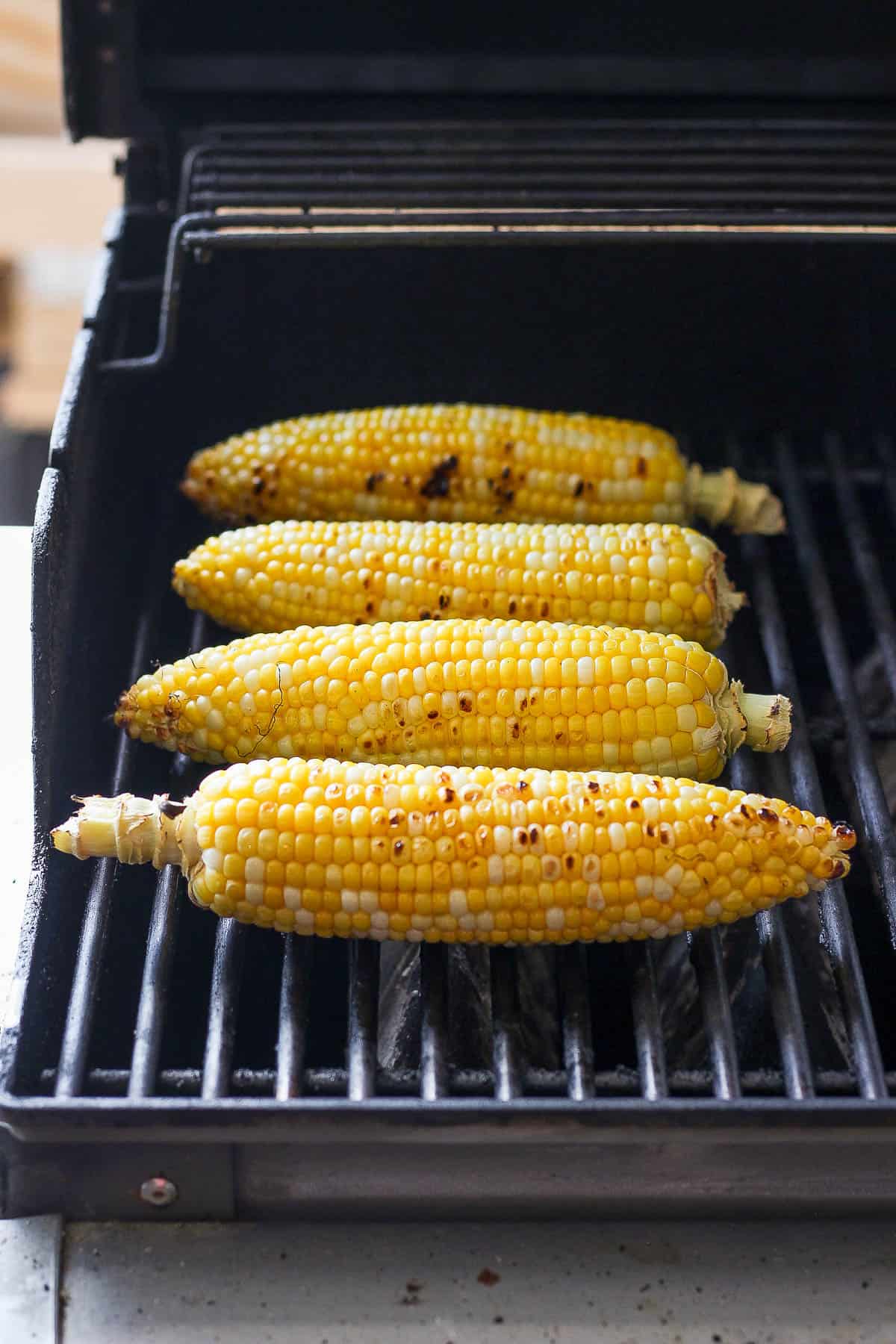 Four pieces of sweet corn on a grill, charred after cooking. 