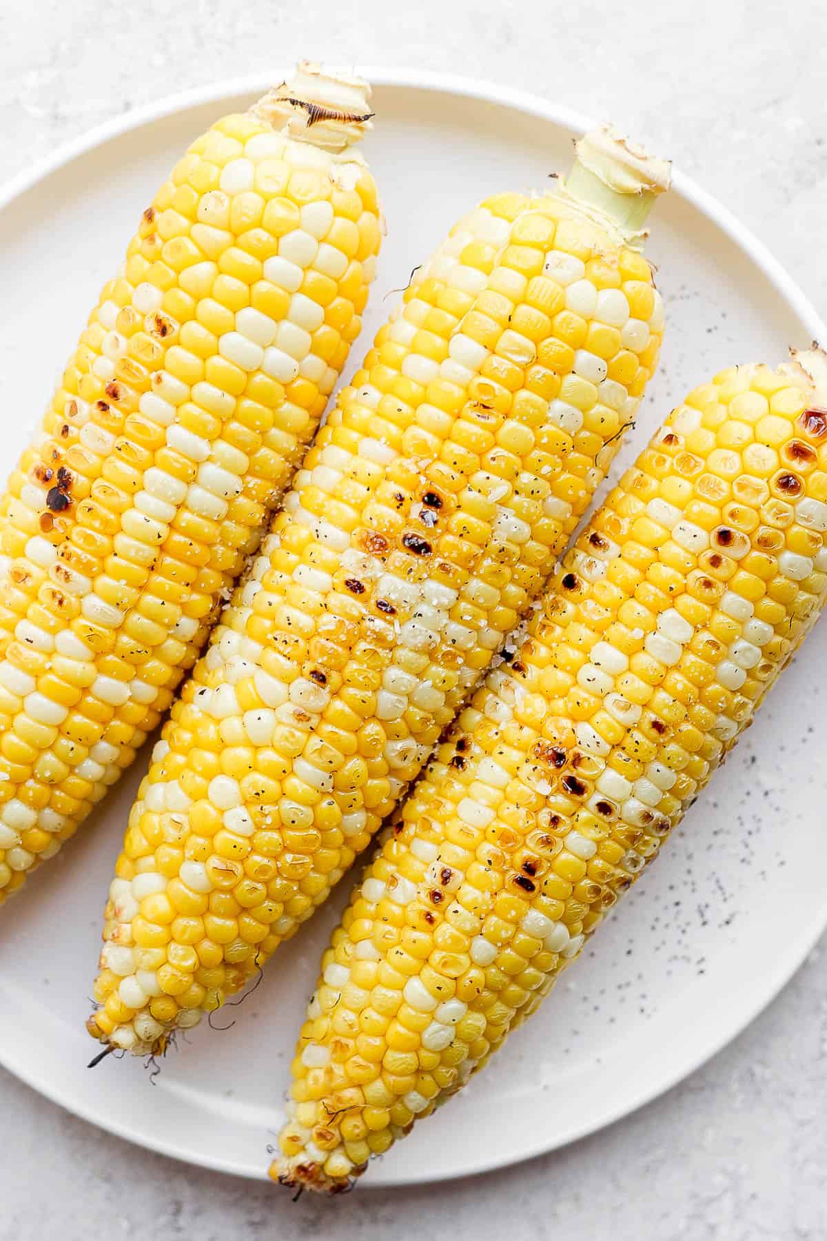 Grilled ears of corn on a white plate.
