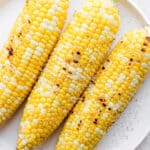 A plate of three grilled pieces of sweet corn.