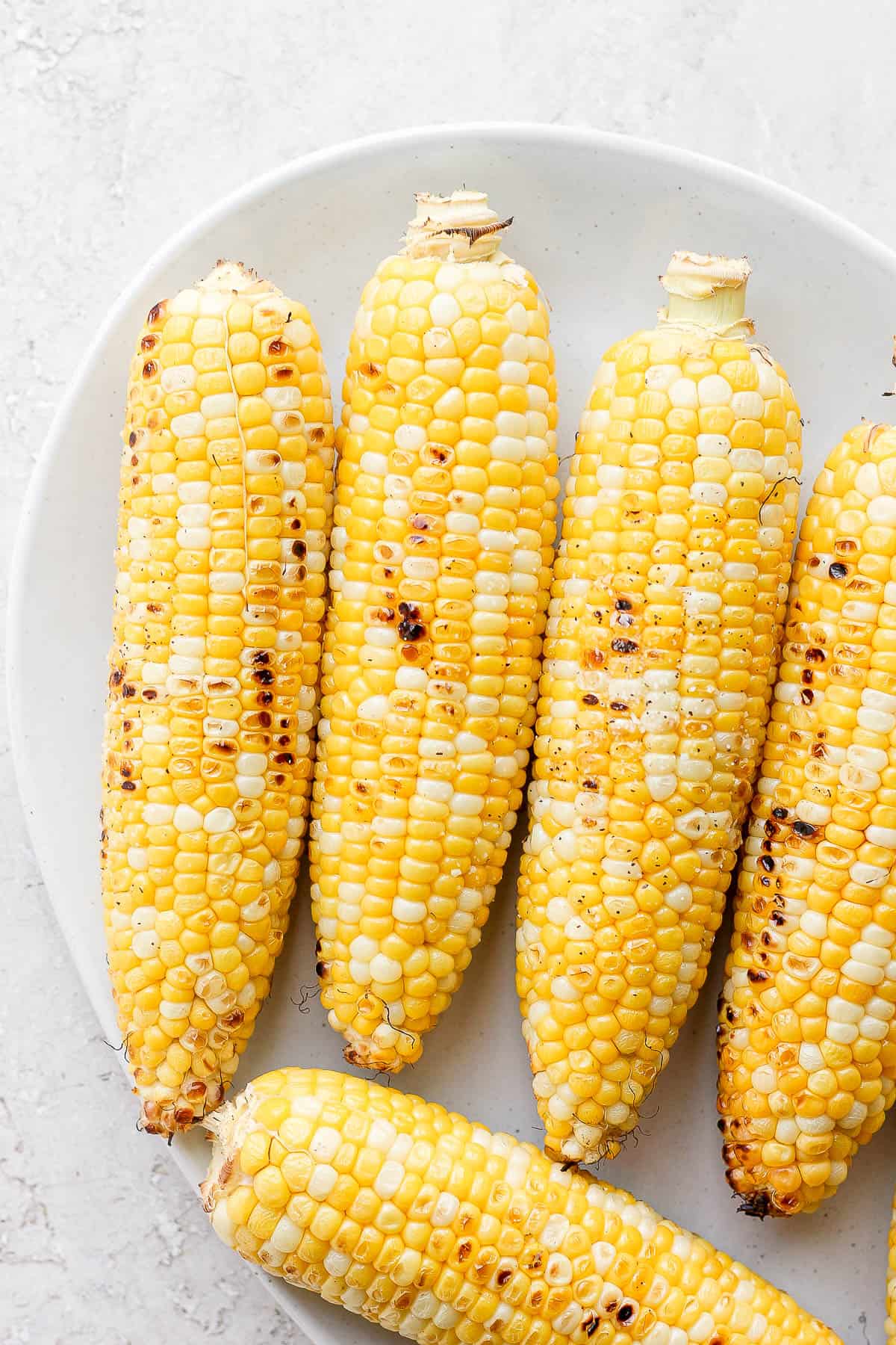 Five pieces of sweet corn on a platter, grilled and charred. 