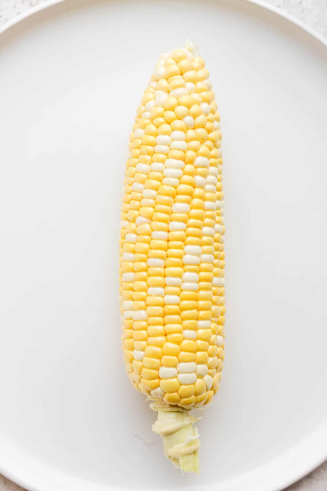 One piece of sweet corn on a plate with husk and silk removed. 