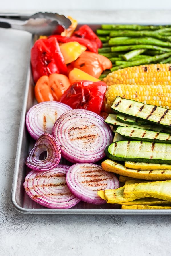 Grilled vegetables on a cookie sheet with tongs.