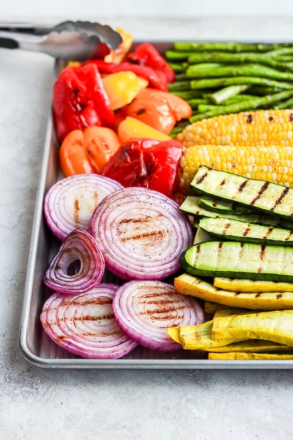 Tongs adding grilled vegetables to a cookie sheet.