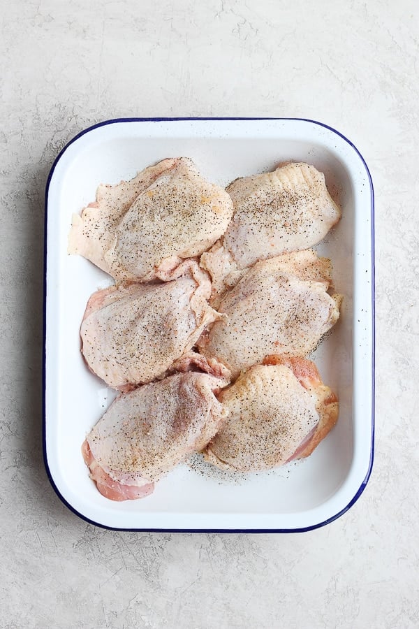 A pan of seasoned, raw bone-in chicken thighs. 