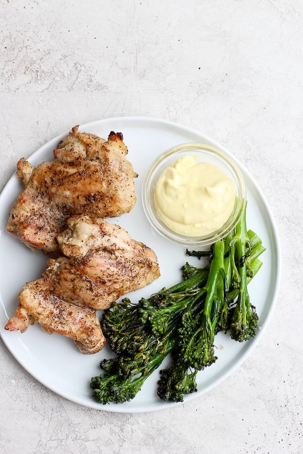 A plate of grilled chicken thighs, boneless, with broccolini and mustard mayo dip. 