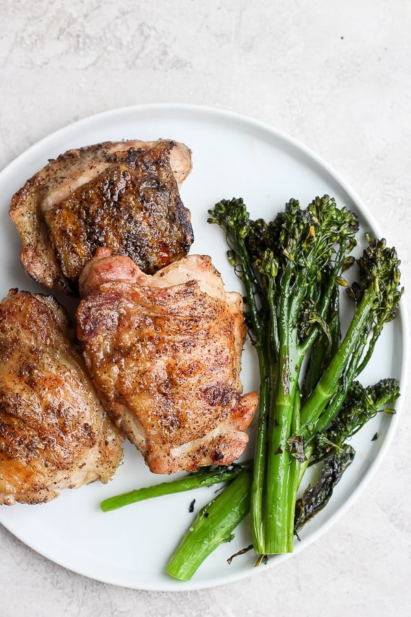 A plate of grilled chicken thighs with some broccolini. 