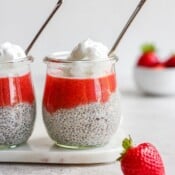 Two jars of strawberry chia pudding with whipped cream on top and spoons sticking out the top.