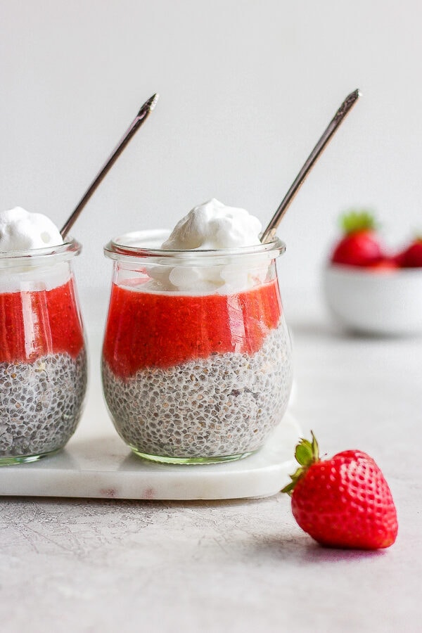 Two jars of strawberry chia pudding with whipped cream on top and spoons sticking out the top.