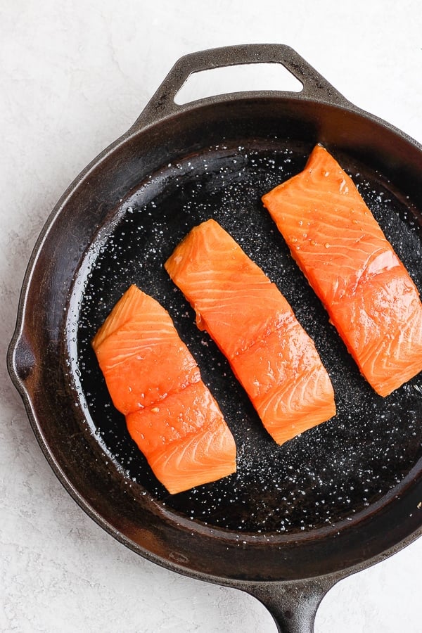 Salmon fillets searing with the skin-side down in a cast iron skillet.
