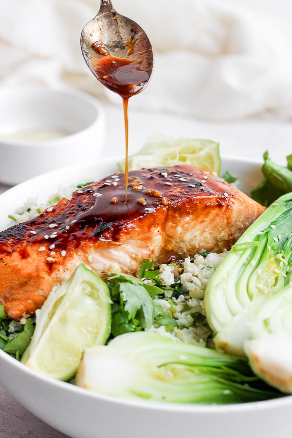 Ginger sesame salmon in a bowl with cilantro lime cauliflower rice, bok choy, and a spoon pouring the sauce on top.