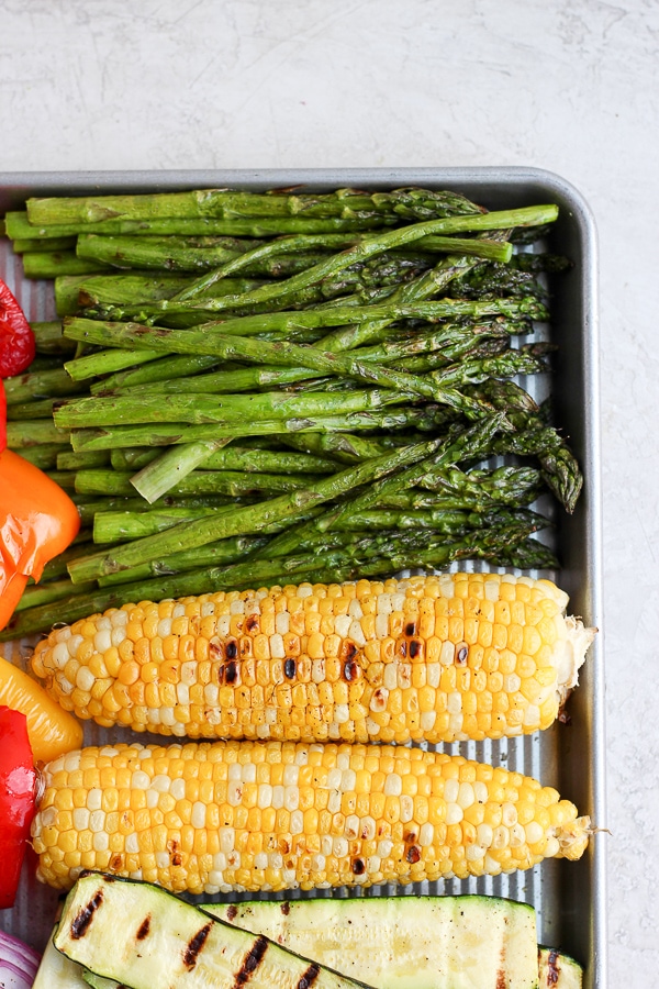 Grilled asparagus on a baking sheet with other baked vegetables.