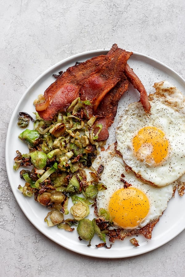 shaved brussel sprouts on a plate with bacon and eggs. 